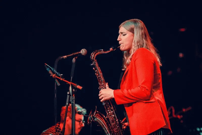 Emma Rawicz playing tenor saxophone in a red jacket