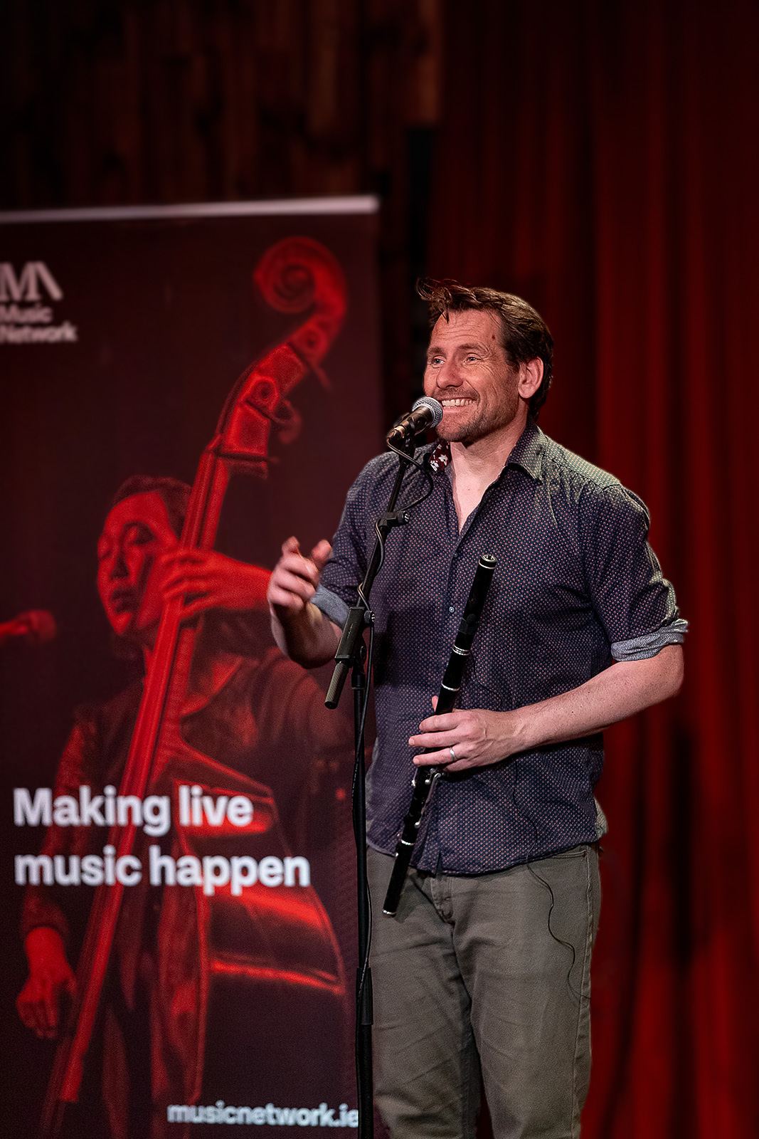 Singing with a wooden flute beside the Music Network banner