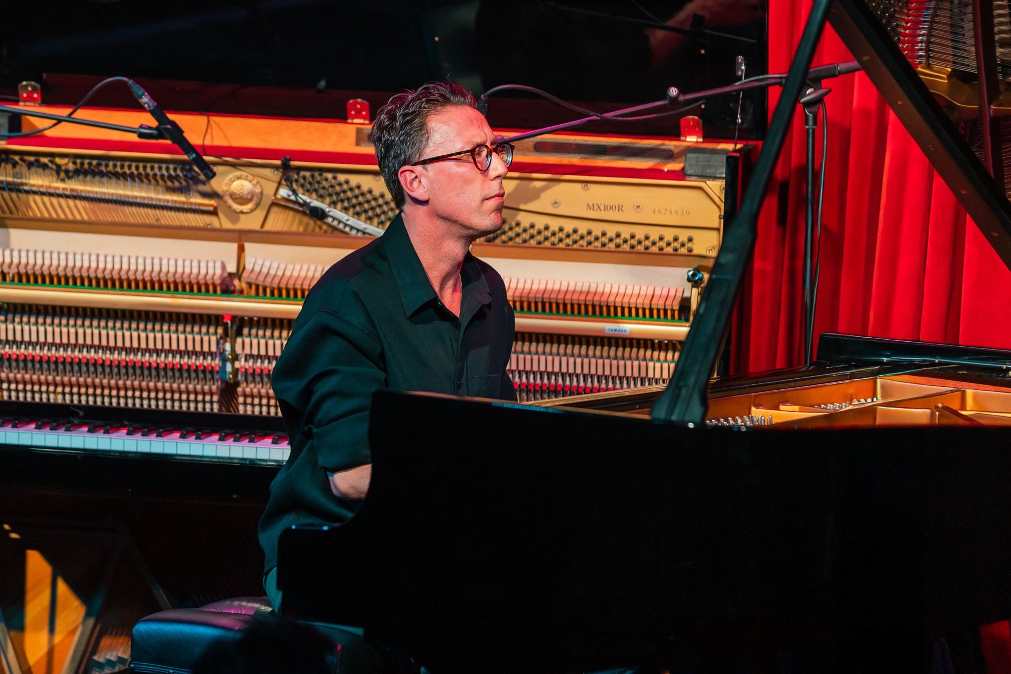 Bill Laurance at the grand piano, the open upright behind him with its hammers bare, red curtain beyond