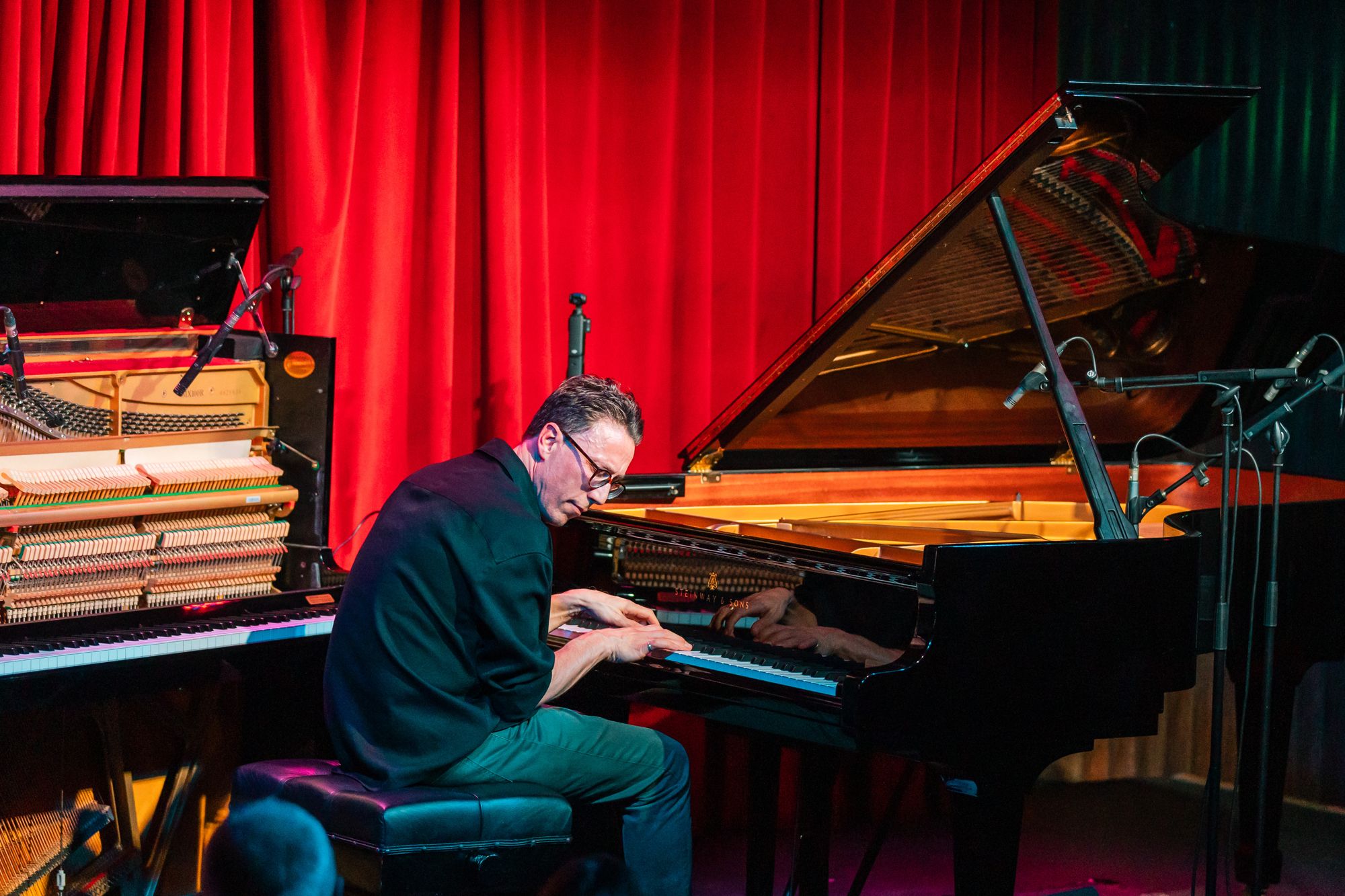 Bill Laurance at the concert grand under red stage light at The Sugar Club, the open upright beside him