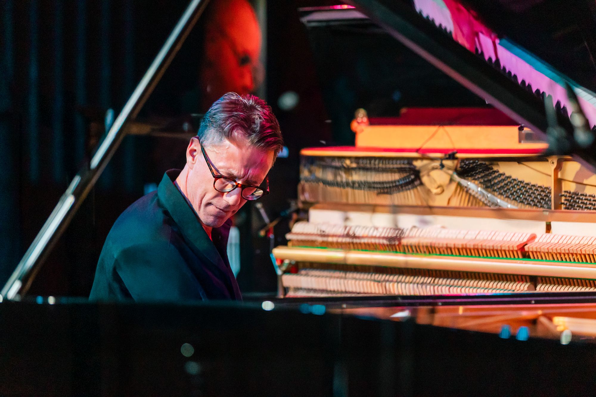 Close on Bill Laurance at the grand, eyes down to the keys, the open upright's hammers glowing behind him