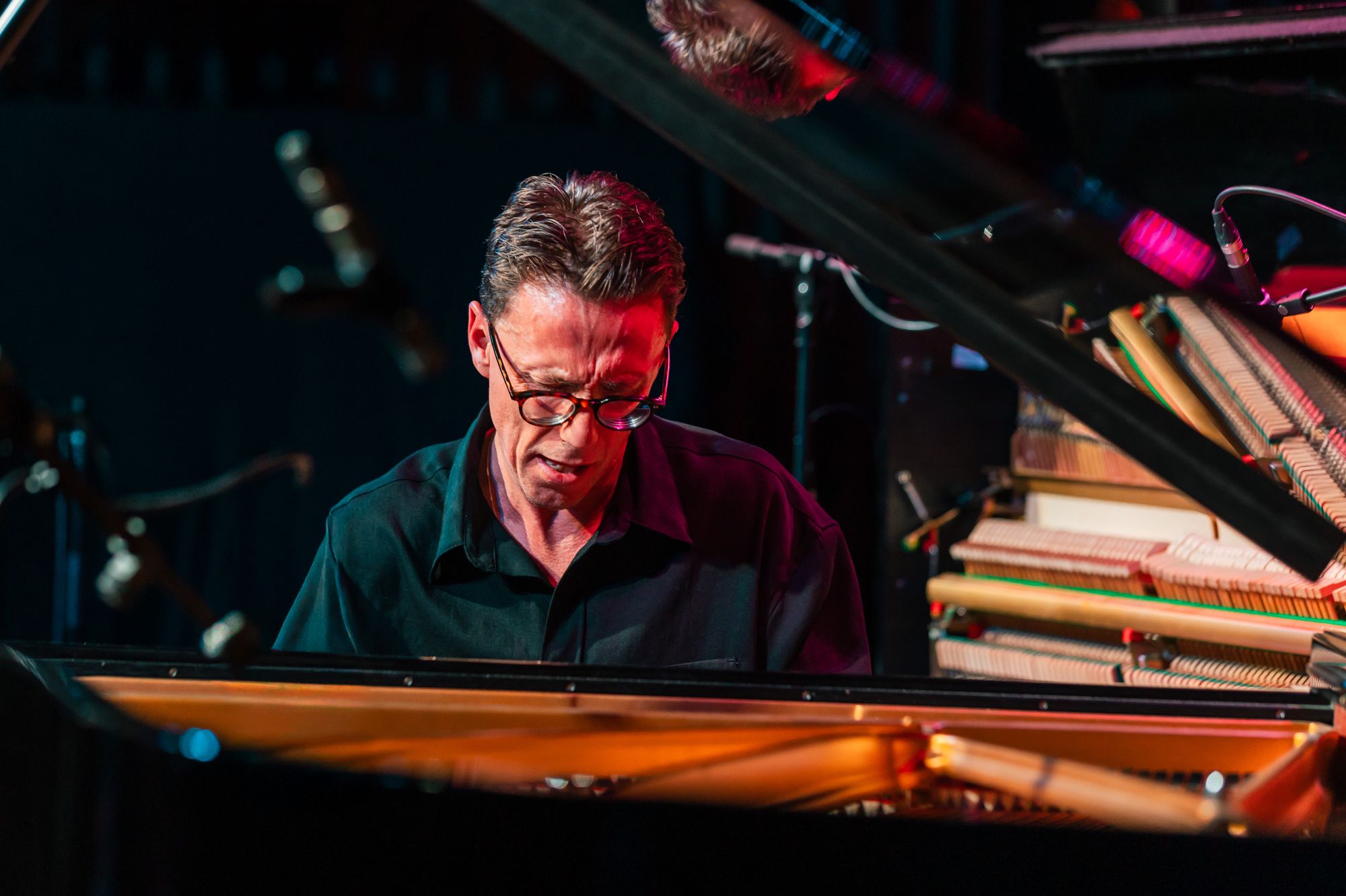 Bill Laurance framed between the grand piano's lid and its gold-lit strings