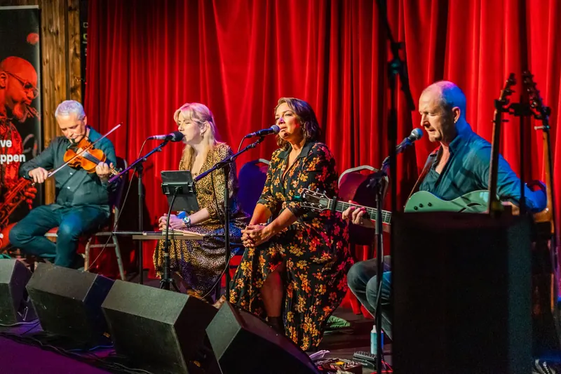 The four musicians seated across the stage of The Sugar Club in front of the red curtain
