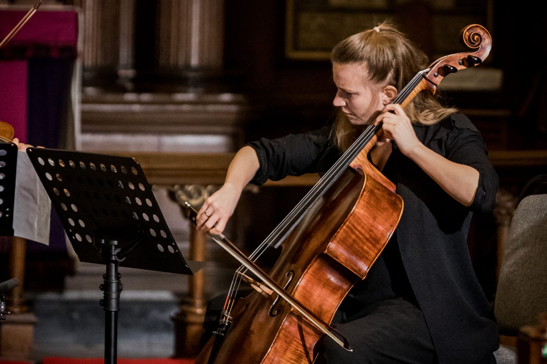 Dóra Kokas at the cello, lit warm against the dark wood of the church
