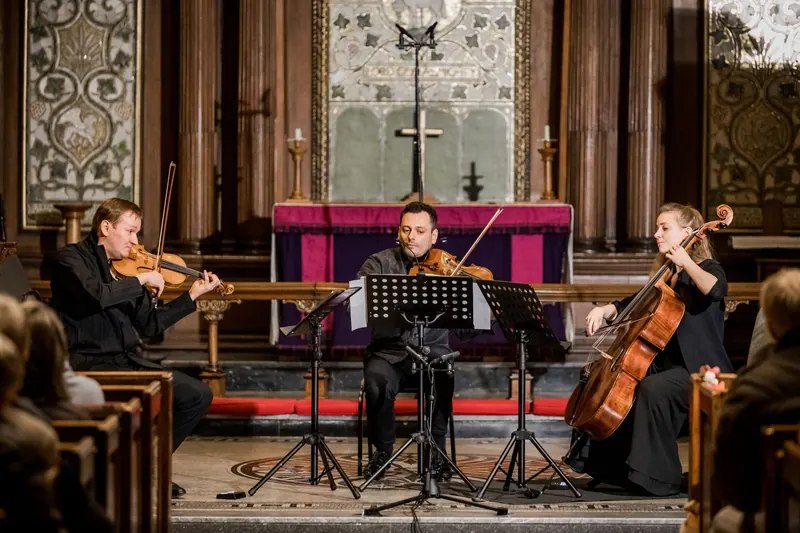 The trio playing in the chancel of St Ann's Church, the cross and decorated reredos behind them and the audience in the pews