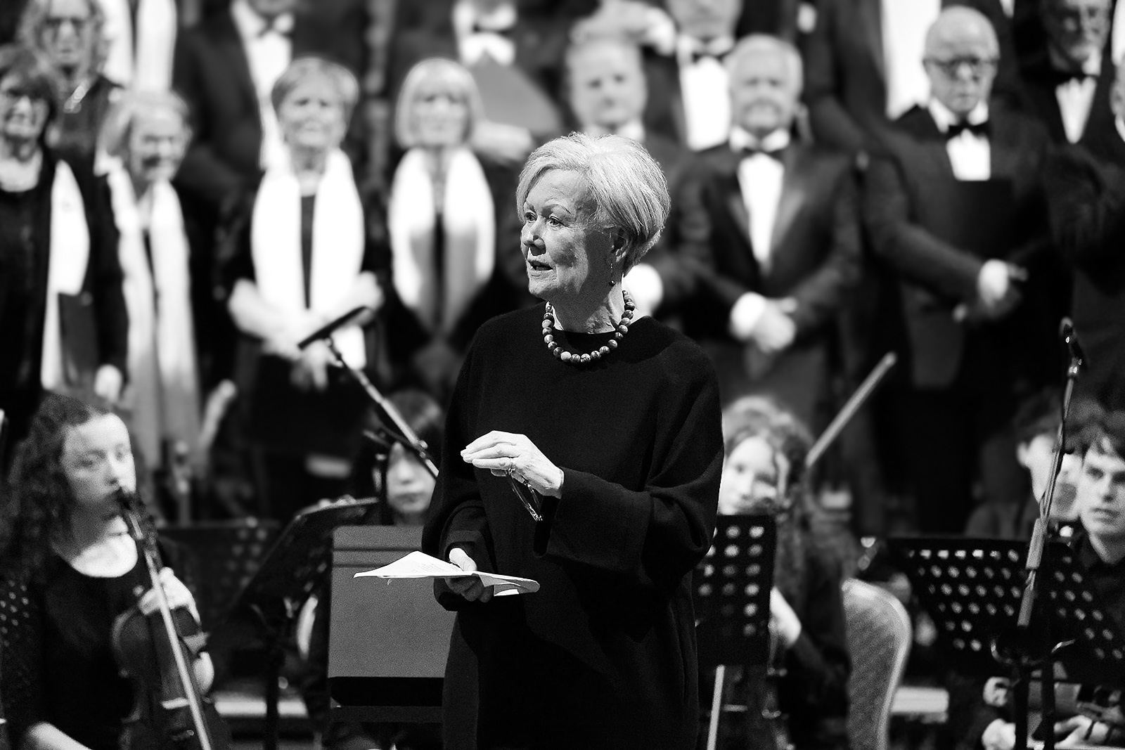 Black and white: a speaker reading to the audience, Setanta Choir standing behind